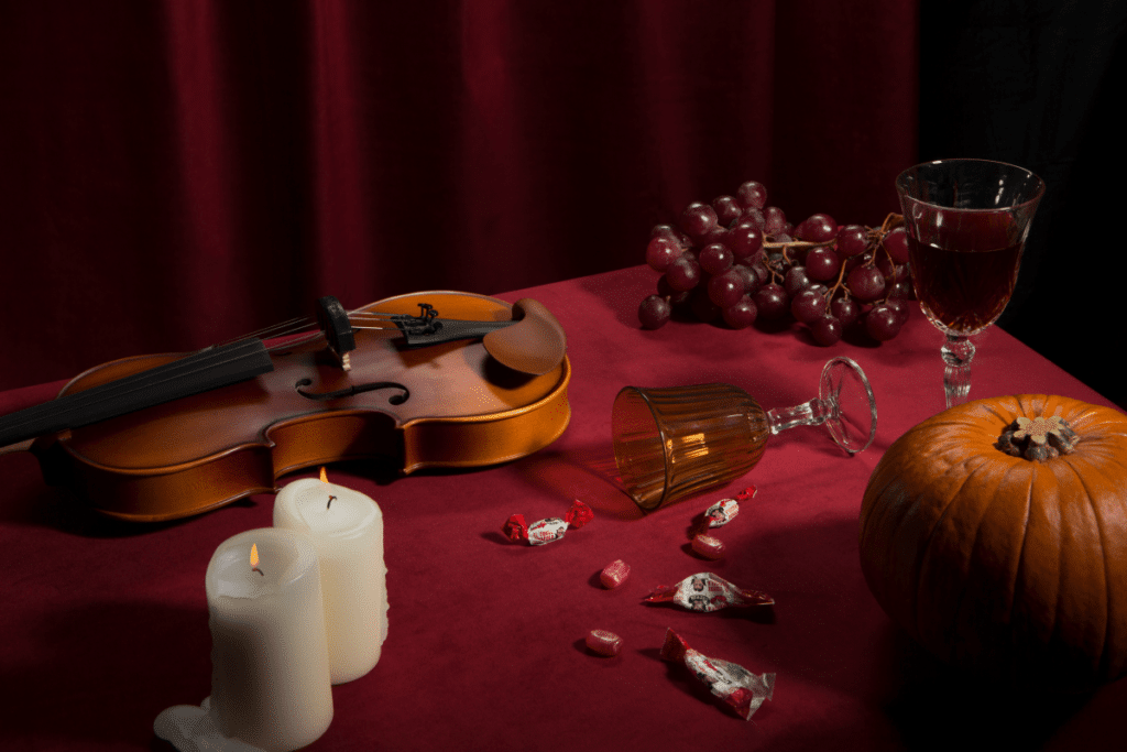 A table displaying candles, violin, grapes, and a knocked over wine glass.