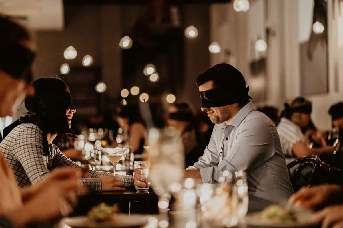 A blindfolded couple smiling at each other at the Dining in the Dark experience.