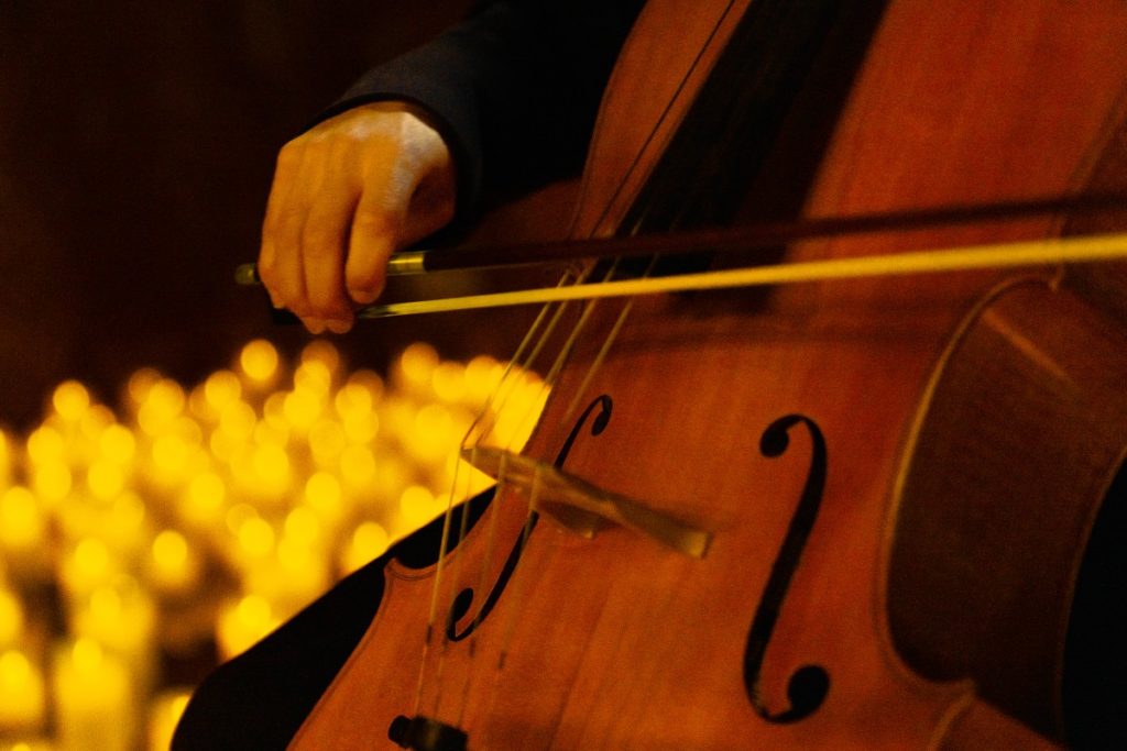 A close up of a person playing the cello with blurred candles in the background