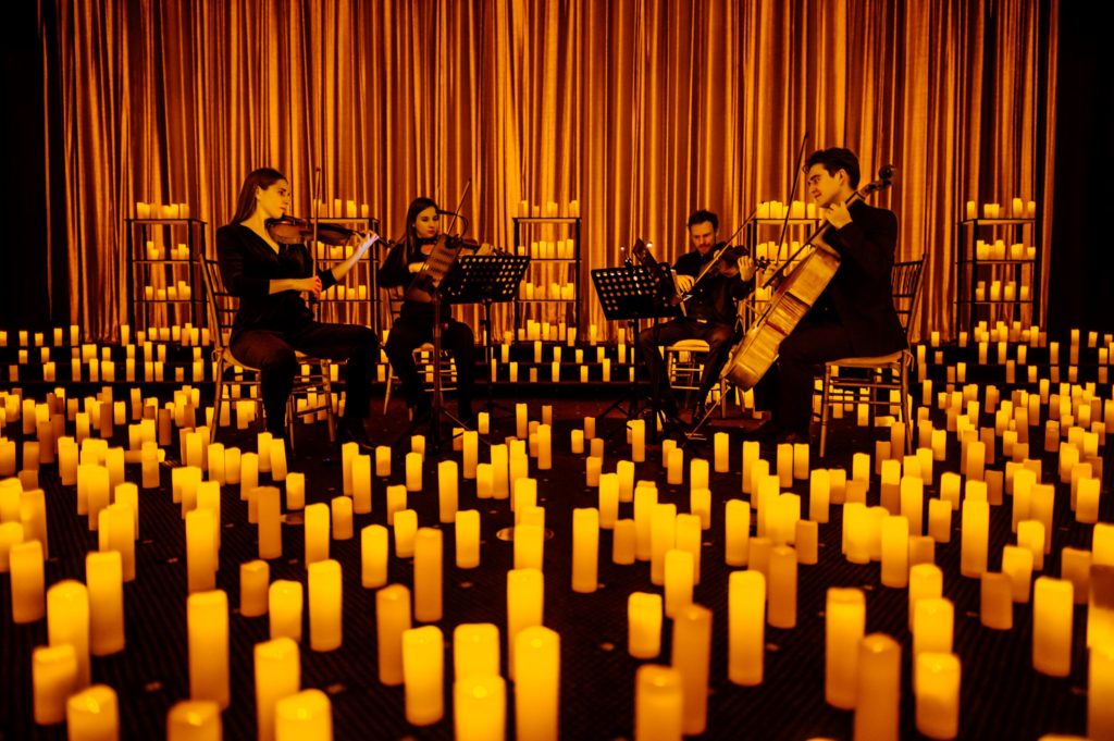 A string quartet performing on a stage surrounded by candles with a heavy curtain drawn in the background at a Candlelight concert.