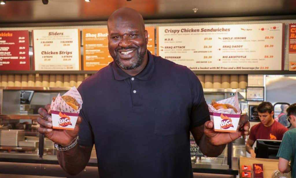Photo of basketball legend Shaquille O'Neal holding chicken sandwiches at one of his Big Chicken locations