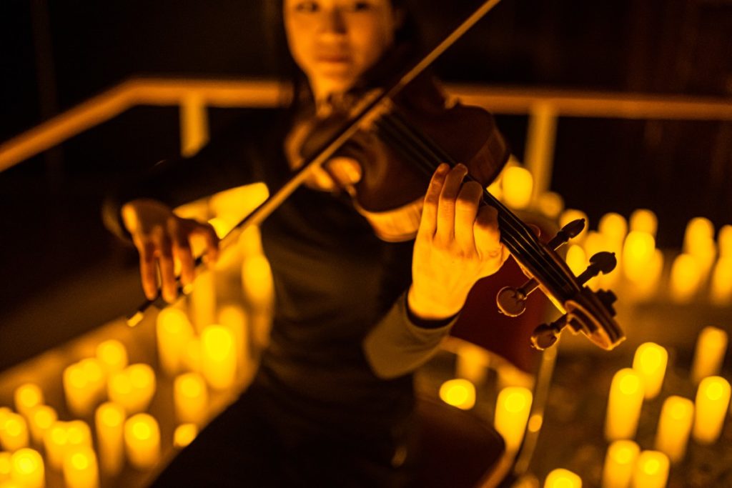 A violinist playing with candles in the background