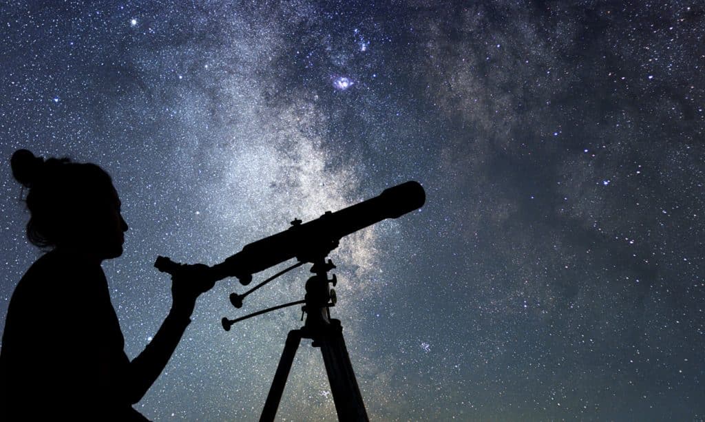 Photo of a woman looking through a telescope at a starry sky during the nighttime