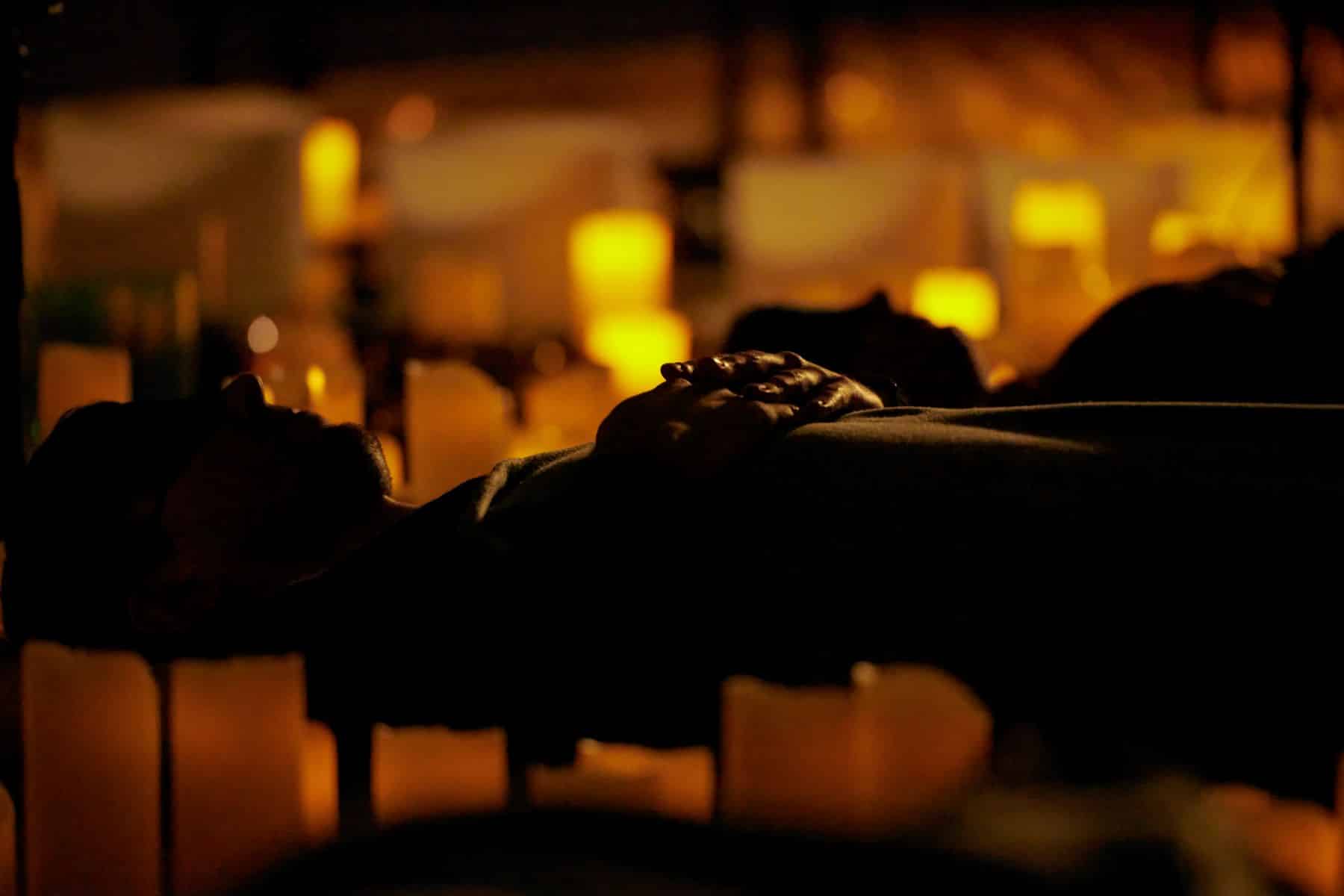 A person lying down at a Mindful Glow experience surrounded by candles.