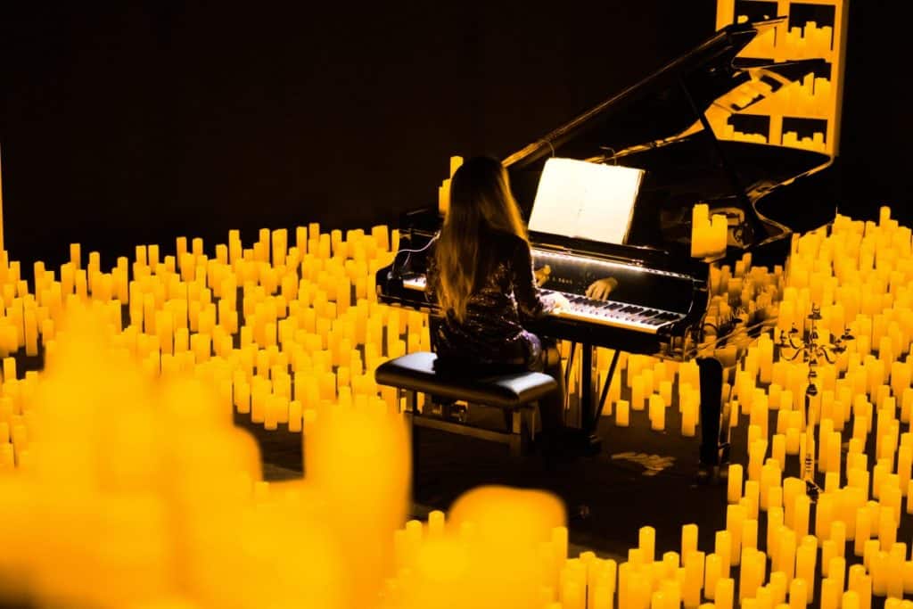 A pianist playing the grand piano on a stage bathed in candlelight